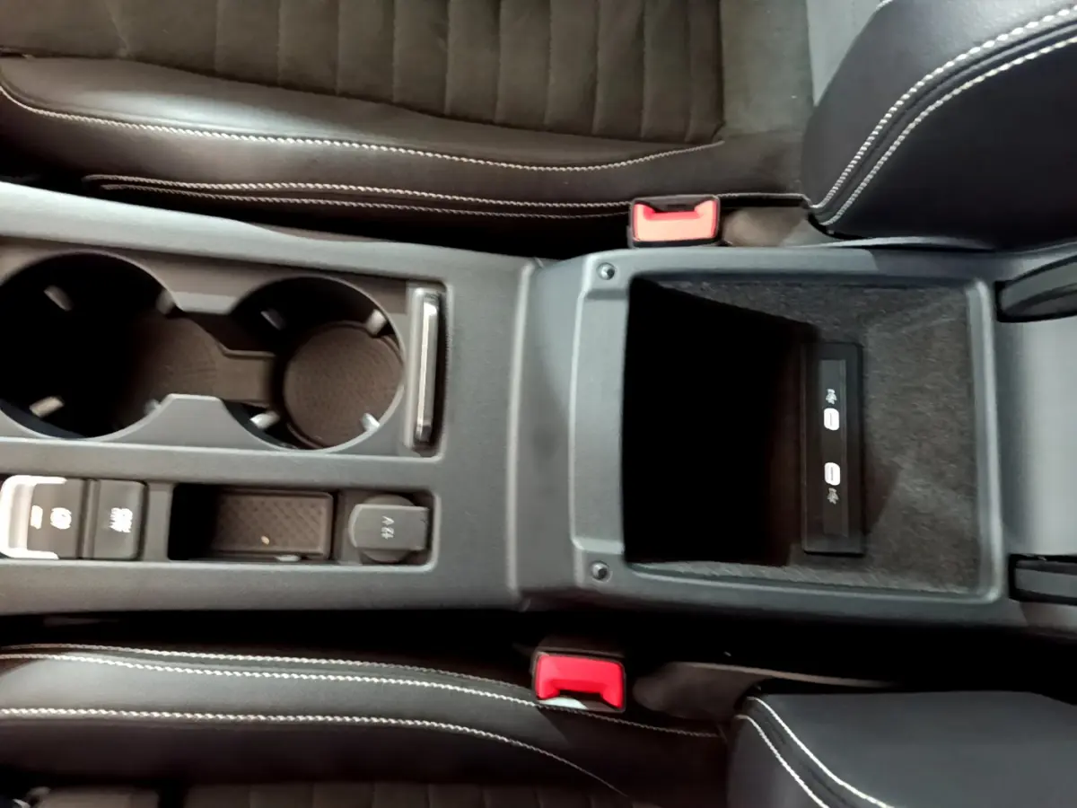 Vue plongeante sur la console centrale noire de la Volkswagen Passat GTE 2022, avec porte-gobelets et rangement USB.