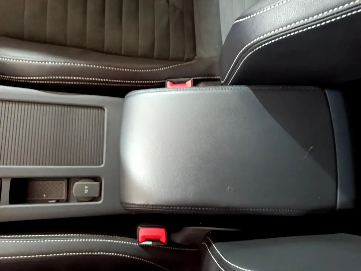 Gros plan sur la console centrale noire avec accoudoir cuir et sièges en tissu gris foncé de la Volkswagen Passat hybride rechargeable.
