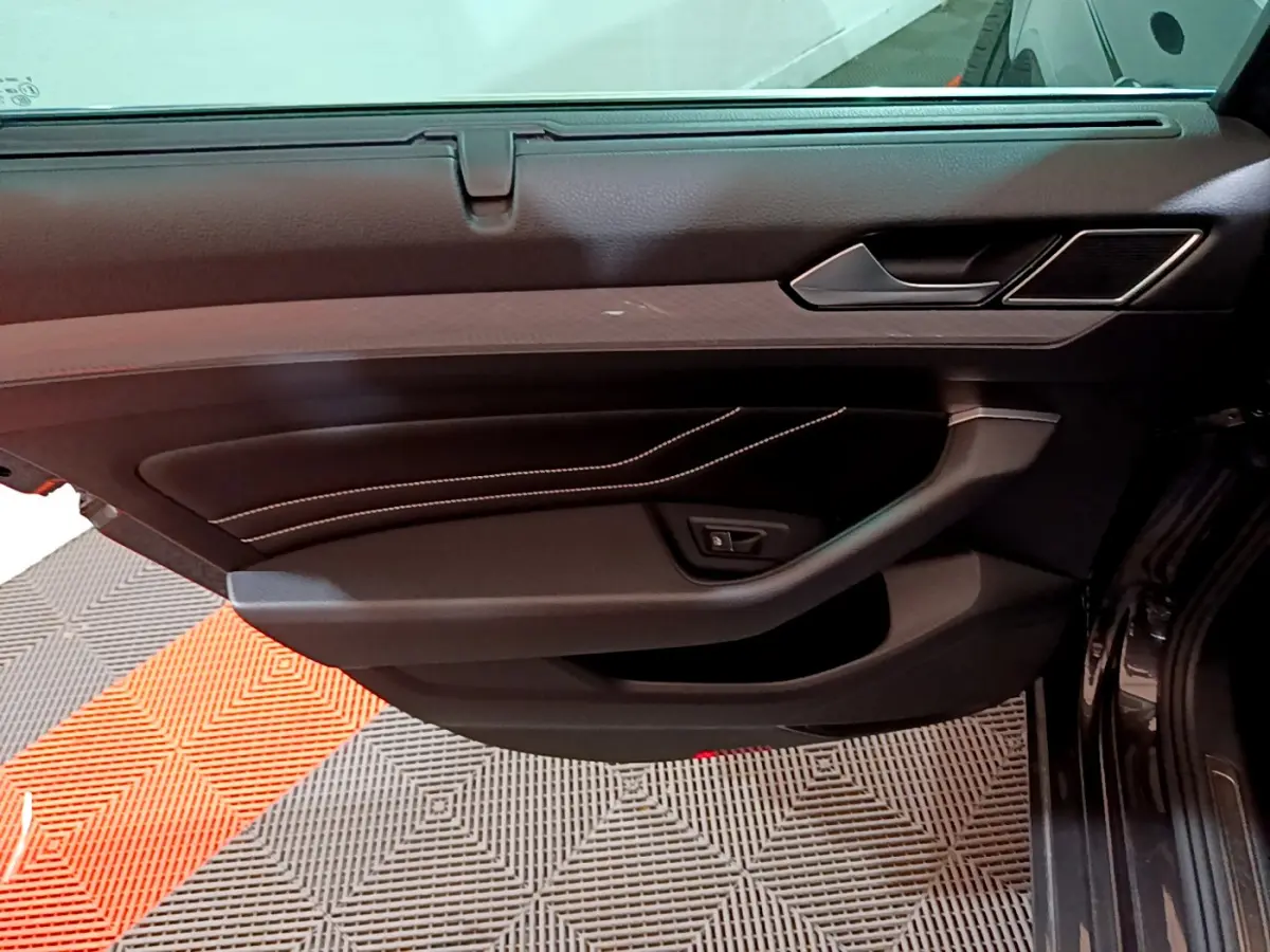 Porte intérieure côté gauche de la Volkswagen Passat GTE 2022 gris foncé, avec surpiqûres blanches et poignée intégrée.