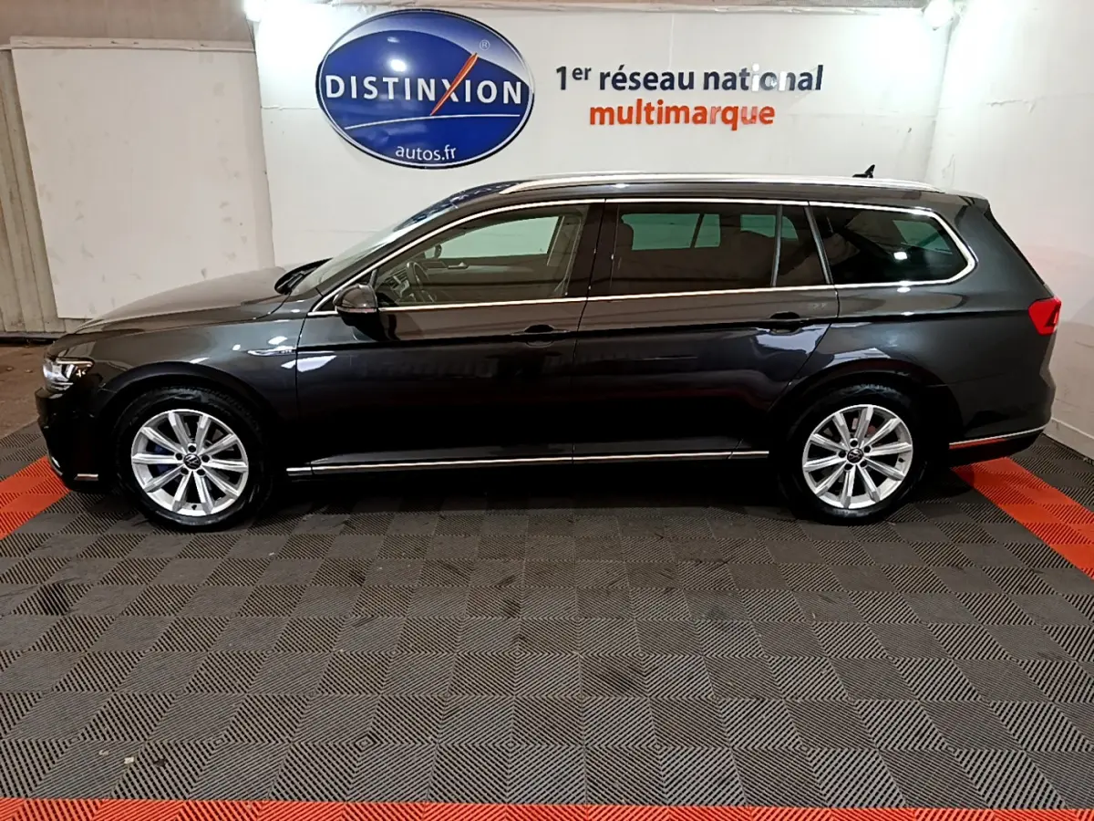 Profil côté gauche d'une Volkswagen Passat SW GTE hybride rechargeable gris foncé dans un showroom multimarque.