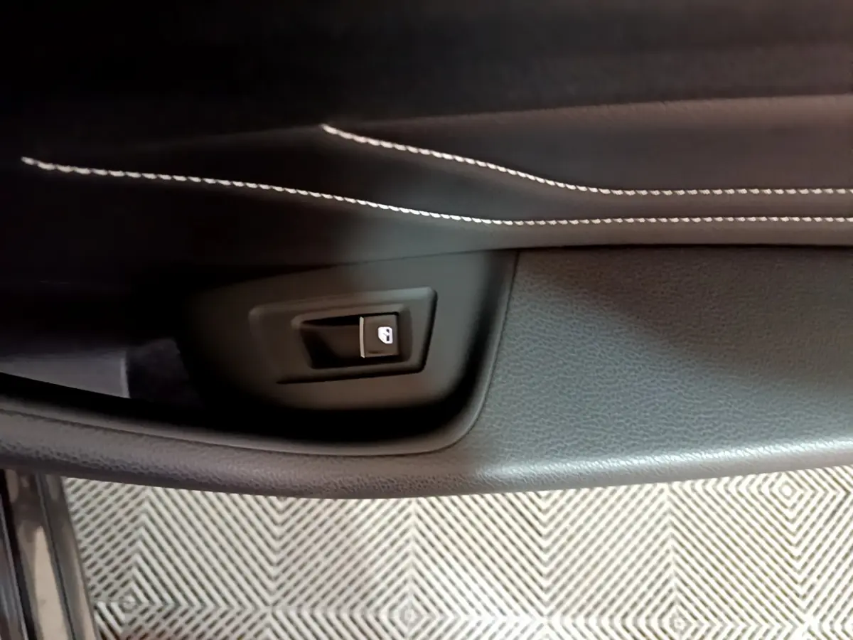 Bouton de déverrouillage de coffre sur la garniture intérieure noire avec surpiqûres blanches d'une Volkswagen Passat GTE hybride rechargeable.