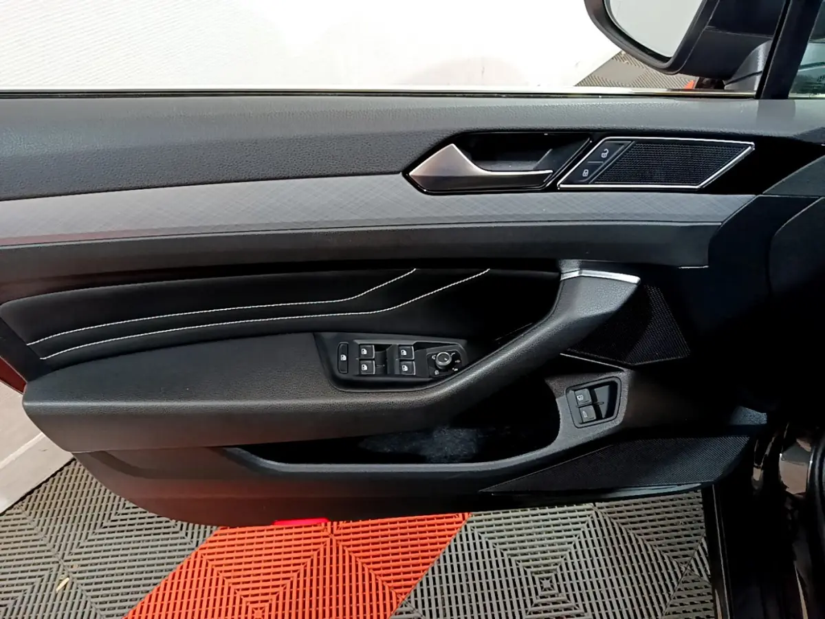 Panneau de porte côté conducteur noir avec commandes électriques et surpiqûres blanches dans une Volkswagen Passat GTE 2022.