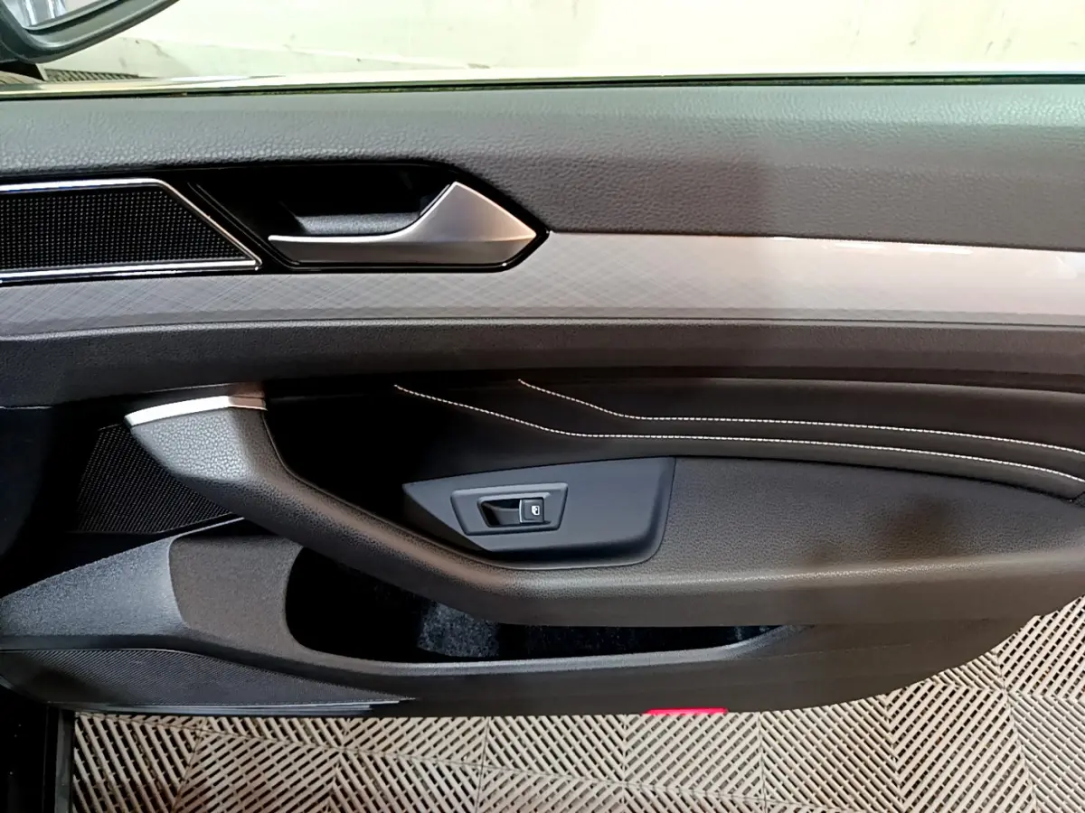 Gros plan sur la porte intérieure côté gauche de la Volkswagen Passat GTE 2022 avec surpiqûres blanches et poignée argentée.