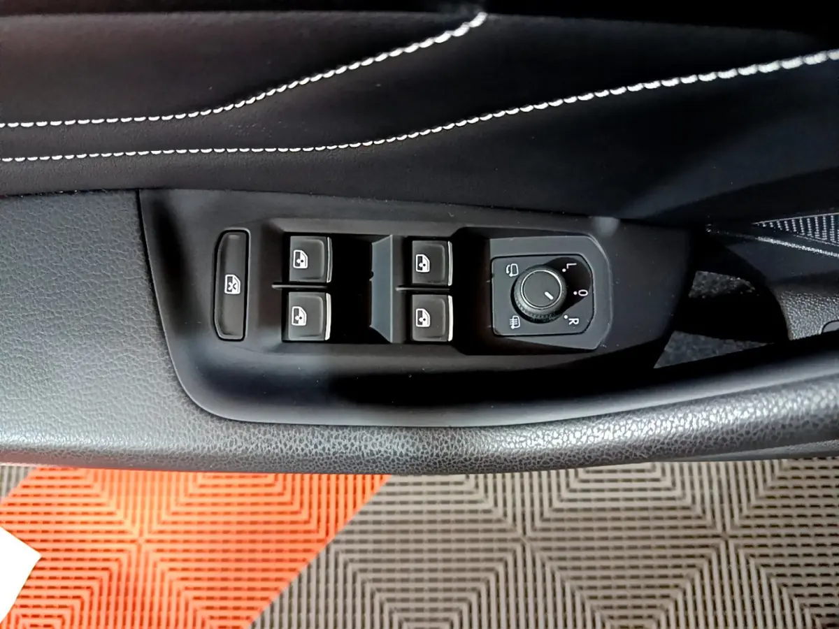 Gros plan sur les commandes de lève-vitres et réglage des rétroviseurs côté conducteur d'une Volkswagen Passat gris foncé 2022.