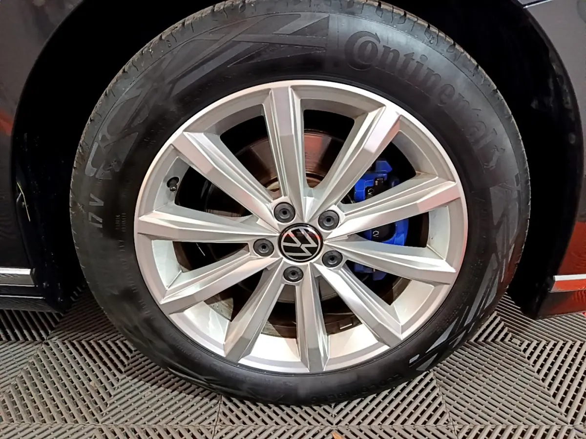 Gros plan sur la roue avant droite d'une Volkswagen Passat gris foncé, avec étrier de frein bleu visible.