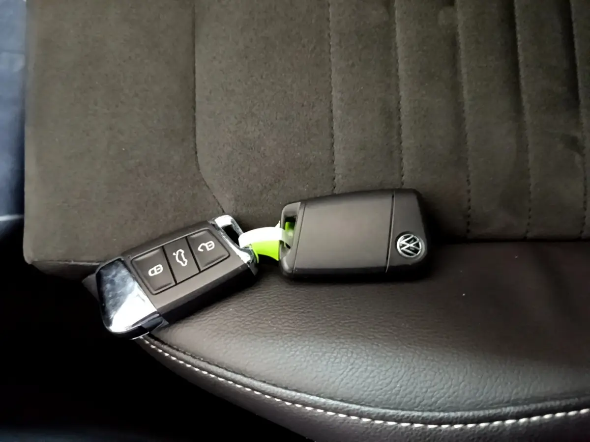 Clé noire Volkswagen posée sur un siège avant en tissu gris foncé et cuir noir avec surpiqûres blanches.