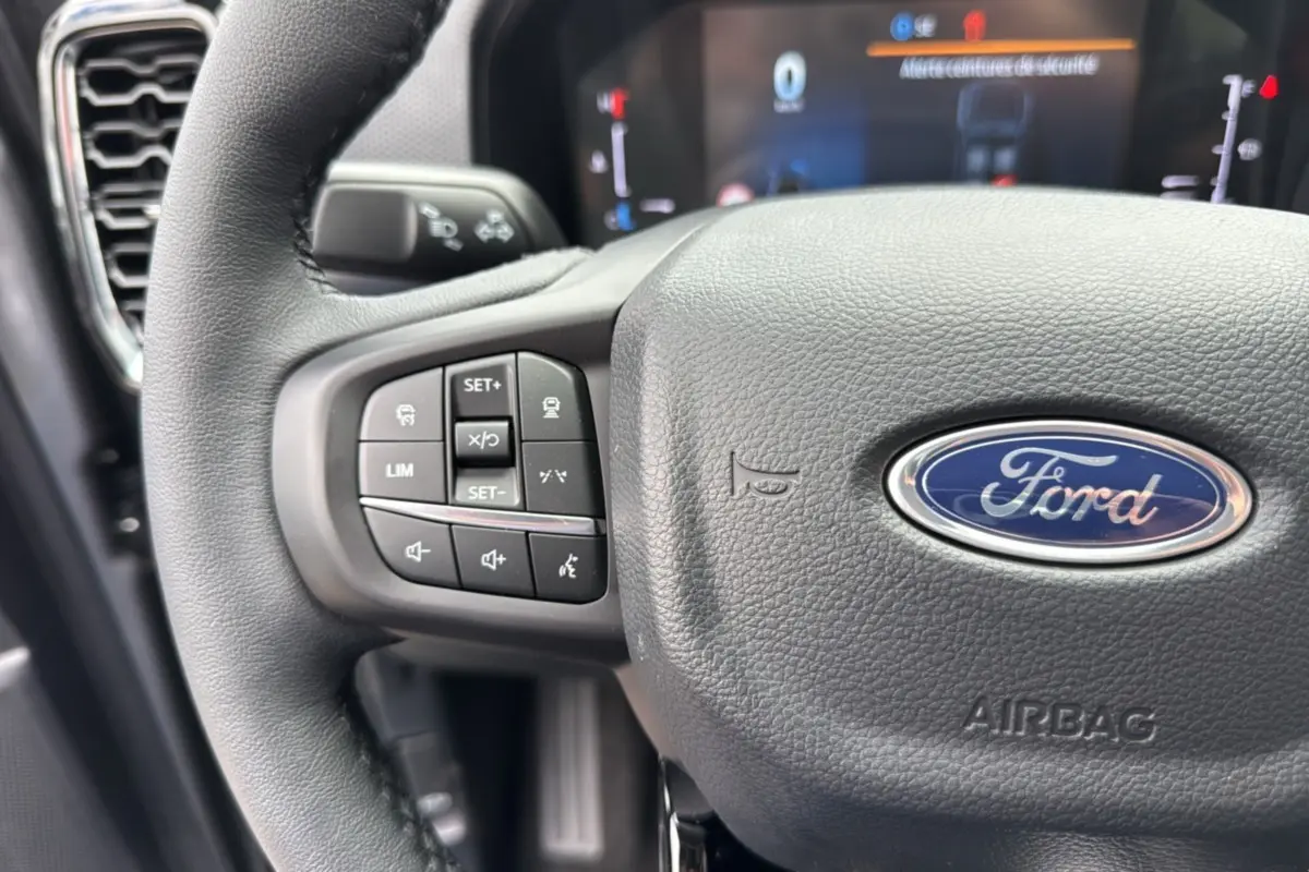 Gros plan sur le volant du Ford Ranger gris carbone 2025 avec commandes intégrées et tableau de bord numérique flou en arrière-plan