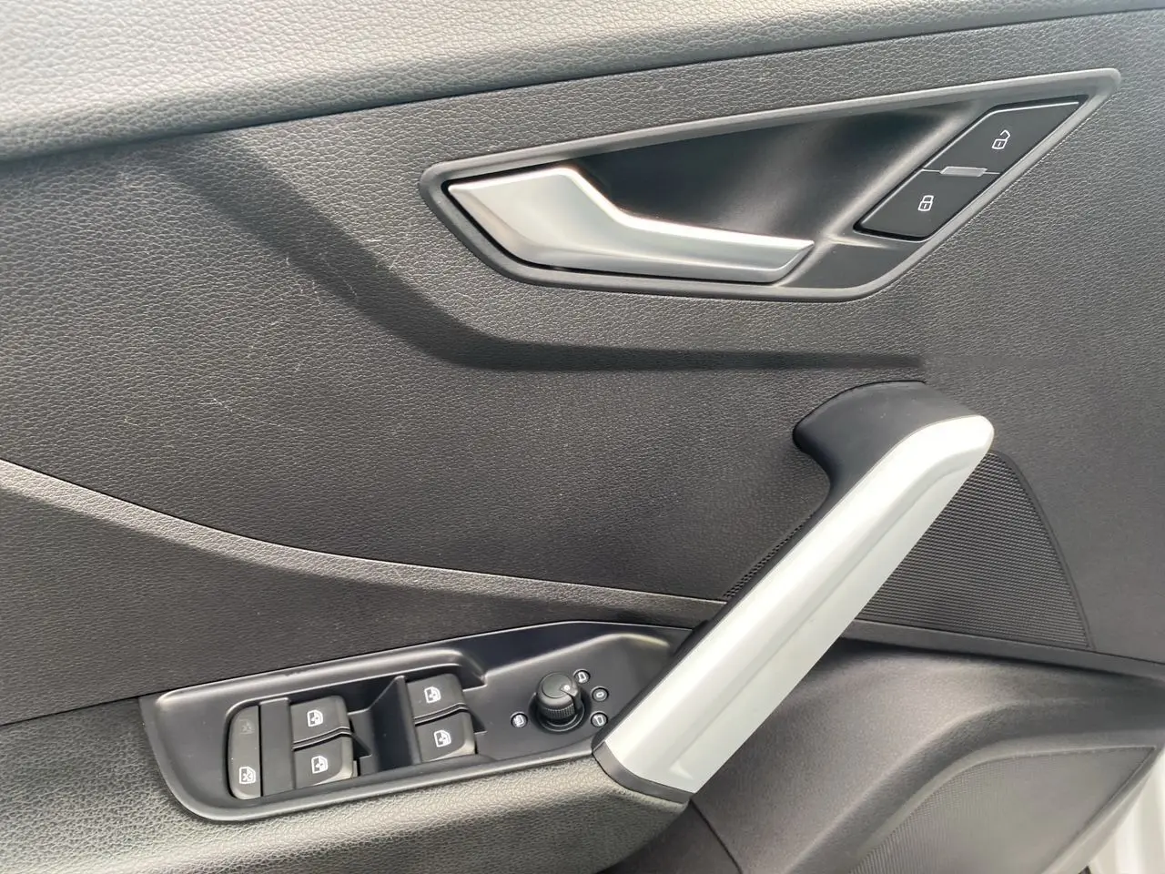 Poignée intérieure côté gauche de porte noire avec commandes de vitres et verrouillage d'une Audi Q2 blanche 2019.