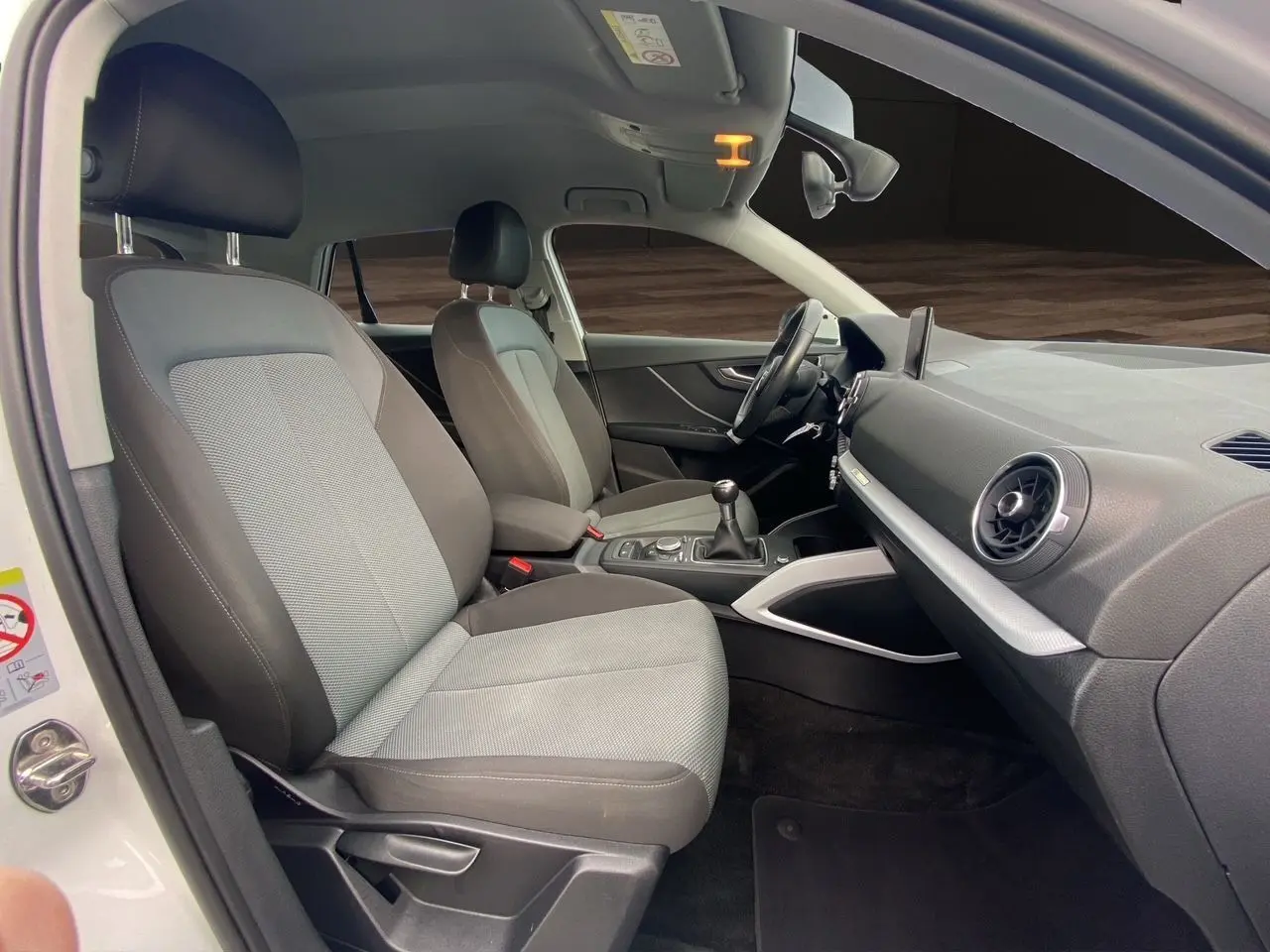 Vue intérieure côté conducteur de l'Audi Q2 blanc 2019, montrant sièges tissu gris et tableau de bord moderne.