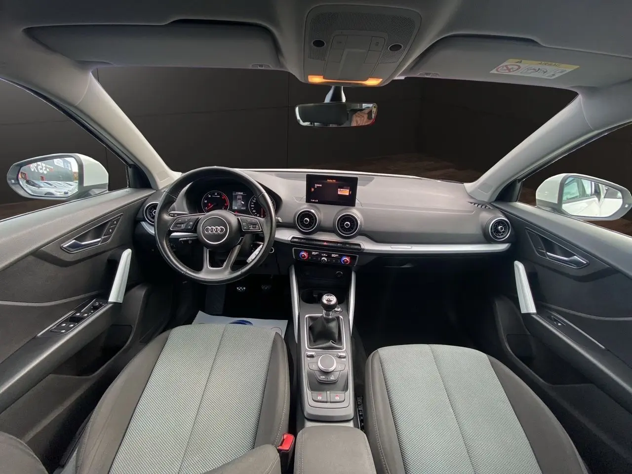 Vue intérieure avant de l'Audi Q2 30 TDI 2019, tableau de bord noir avec volant multifonction et sièges tissu gris.