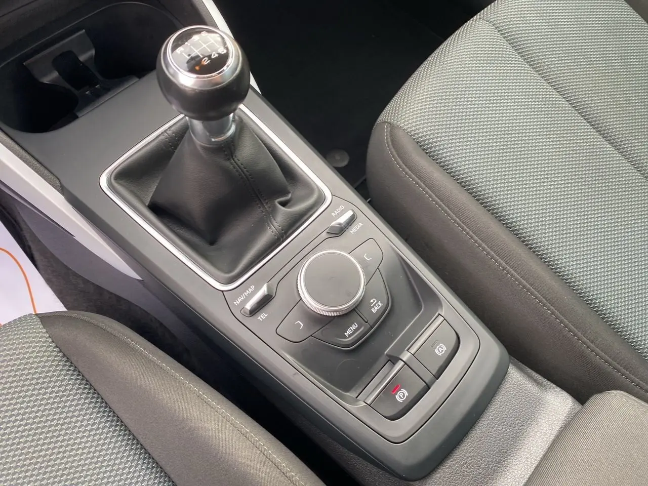 Vue rapprochée de la console centrale noire avec levier de vitesses manuel et sièges tissu gris de l'Audi Q2 blanc.