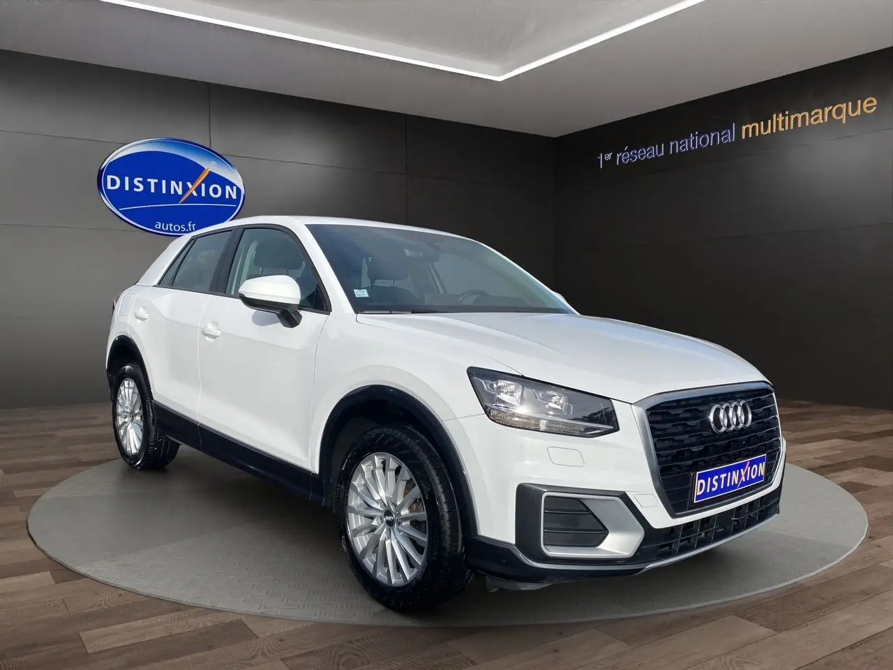 Audi Q2 blanc vue 3/4 avant droit, avec calandre noire et jantes alliage argentées, en showroom intérieur.