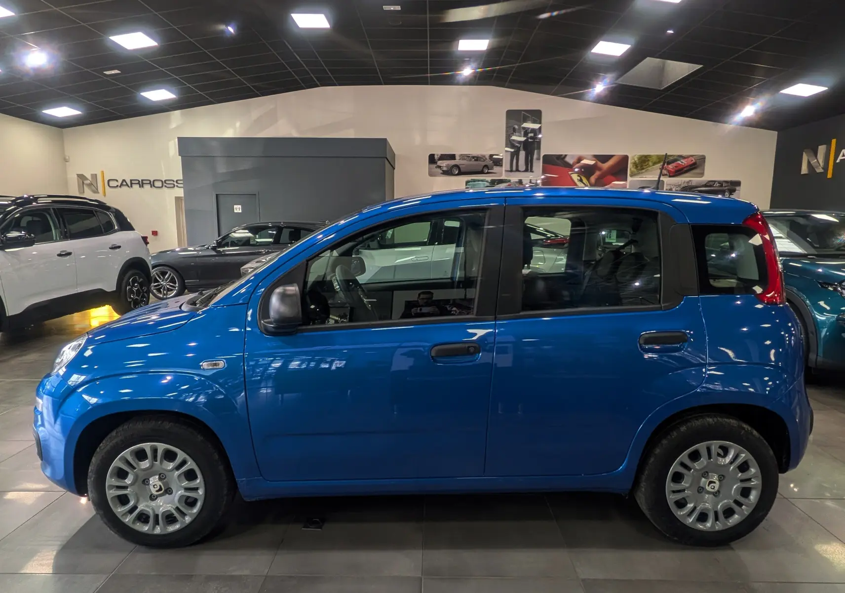 Vue de profil côté gauche d'une Fiat Panda 1.0 Hybrid 2025 en Bleu Italia, compacte et urbaine dans un showroom.