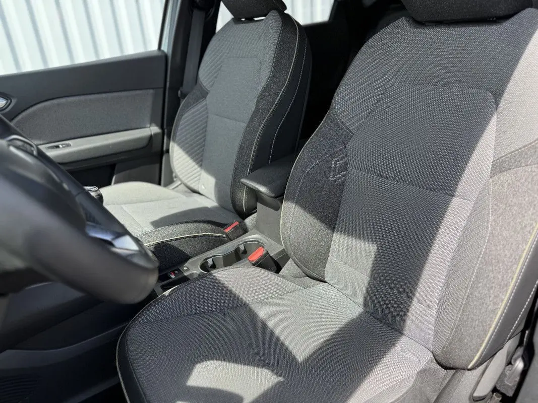 Vue intérieure rapprochée des sièges avant gris du Renault Captur 2025, mettant en valeur les textures et accoudoir central.