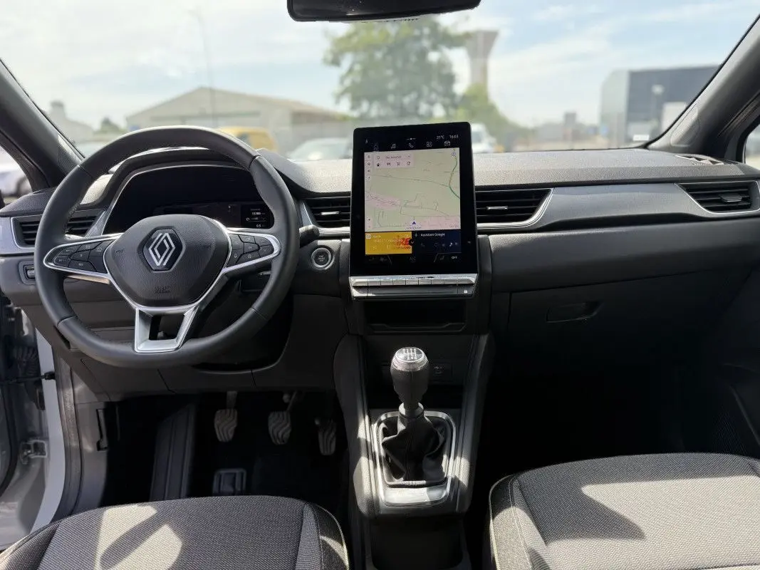 Vue intérieure avant du Renault Captur 2025, tableau de bord noir avec écran tactile vertical et levier de vitesse manuel.