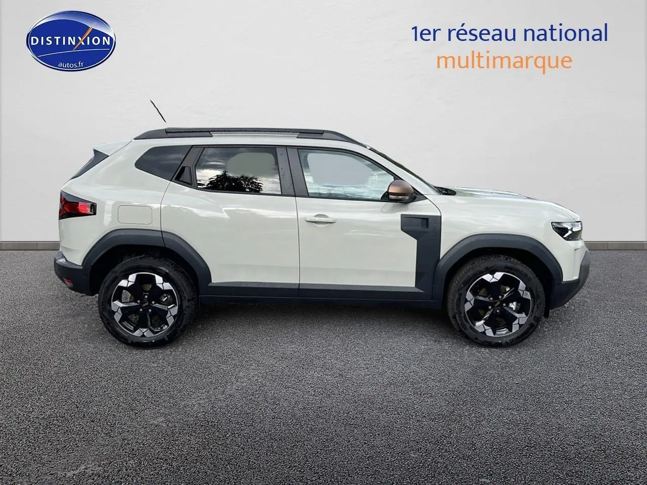 Profil droit du Dacia Duster 2025 Sandstone avec barres de toit et jantes noires semi-diamantées.