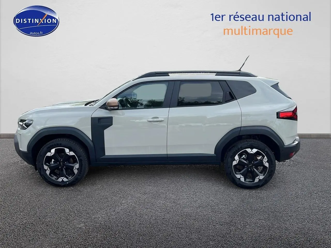 Vue de profil côté gauche du Dacia Duster 2025 Sandstone avec barres de toit et jantes 18 pouces noires et argentées.