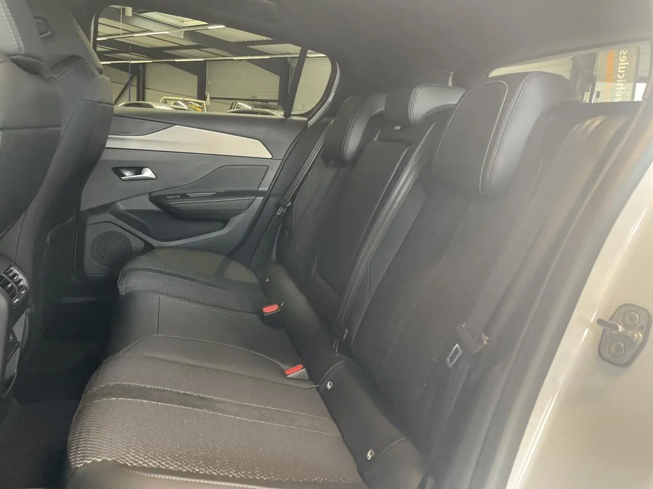 Vue intérieure côté droit sur la banquette arrière noire de la Peugeot 308 blanche avec surpiqûres et ceintures visibles.