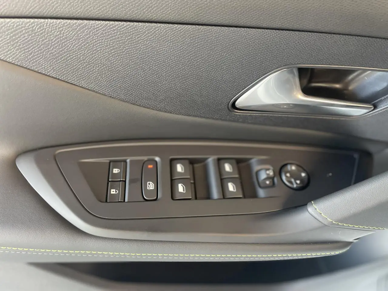 Gros plan sur la commande des vitres côté gauche d'une Peugeot 308 blanche, avec surpiqûres vertes sur la garniture.