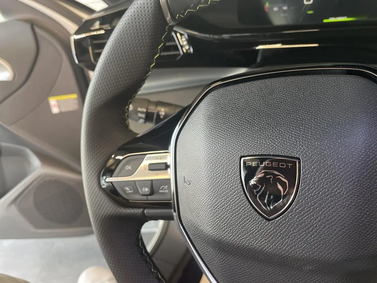 Gros plan sur le volant cuir noir perforé avec logo Peugeot et commandes intégrées dans une Peugeot 308 blanche 2025.