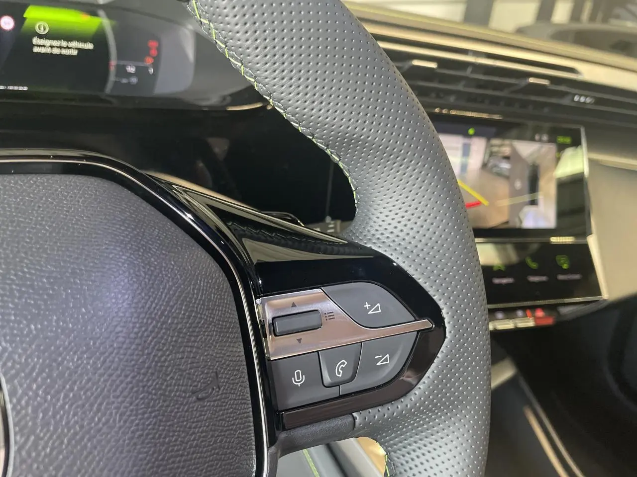Gros plan sur le volant cuir perforé gris avec surpiqûres vertes et commandes multifonctions d'une Peugeot 308 blanche.