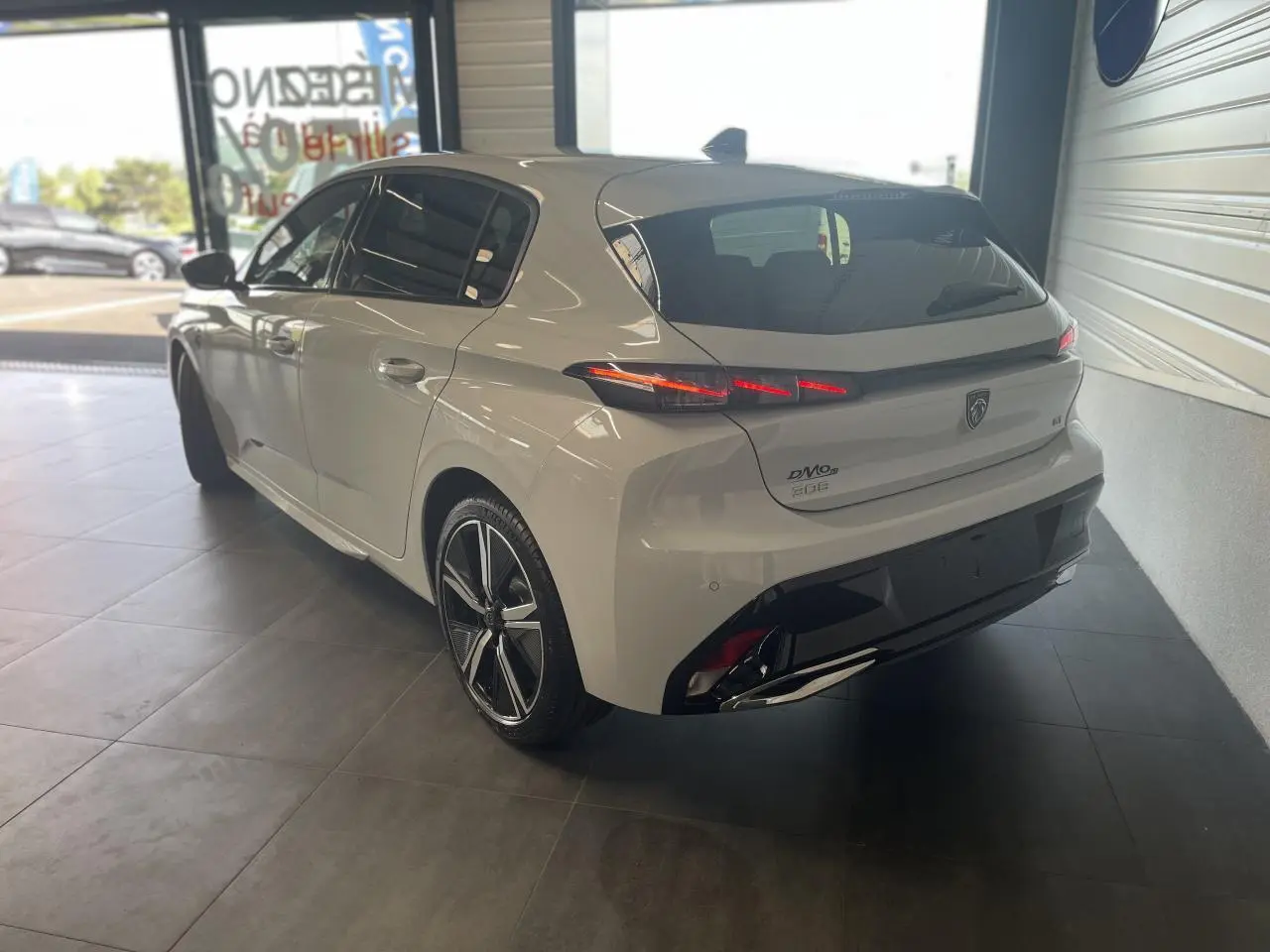 Peugeot 308 blanche vue 3/4 arrière droit en intérieur, avec feux arrière LED et jantes alliage noires.