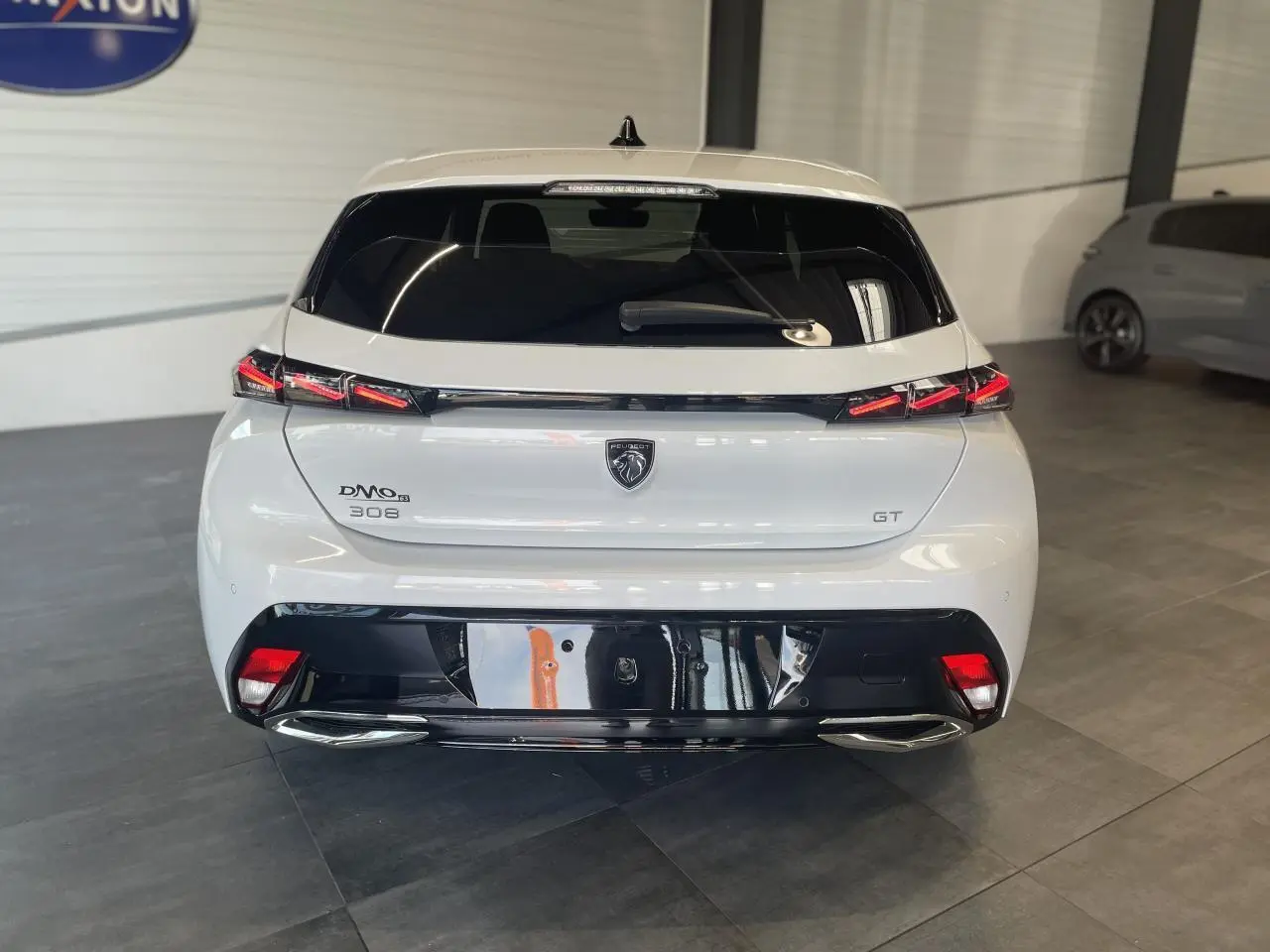 Vue arrière d'une Peugeot 308 GT blanche avec feux arrière en griffe et diffuseur noir brillant.