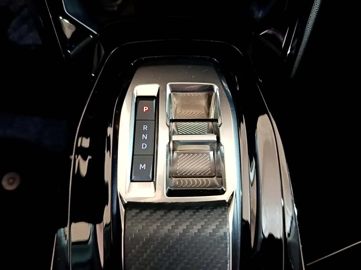 Gros plan sur la console centrale noire brillante avec sélecteur de boîte auto et commandes en finition carbone.