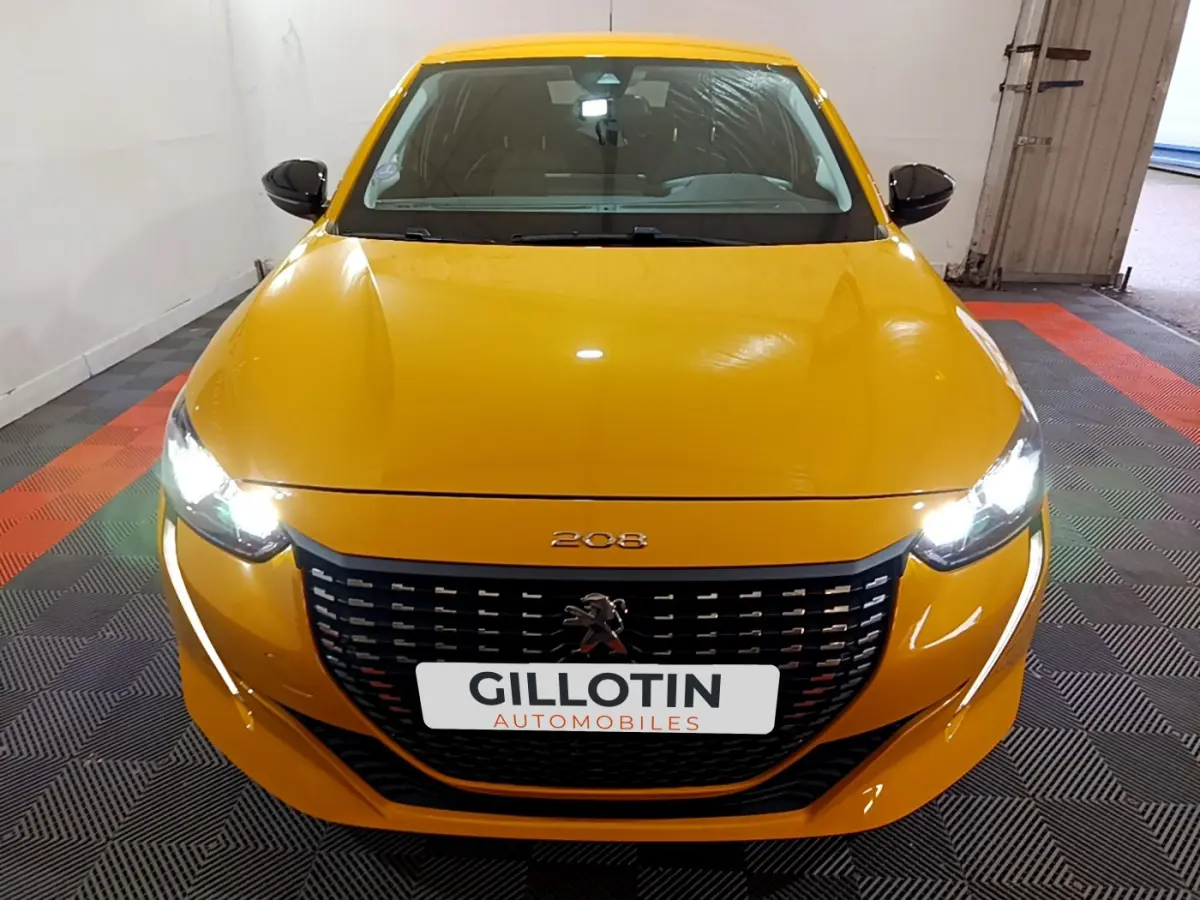 Peugeot 208 jaune vue de face avec phares allumés et calandre noire distinctive dans un garage.