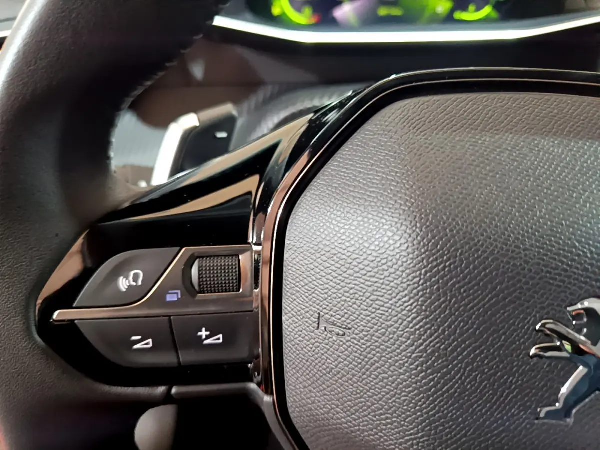 Gros plan sur le volant cuir noir de la Peugeot 208 jaune, avec commandes audio et logo lion visible.