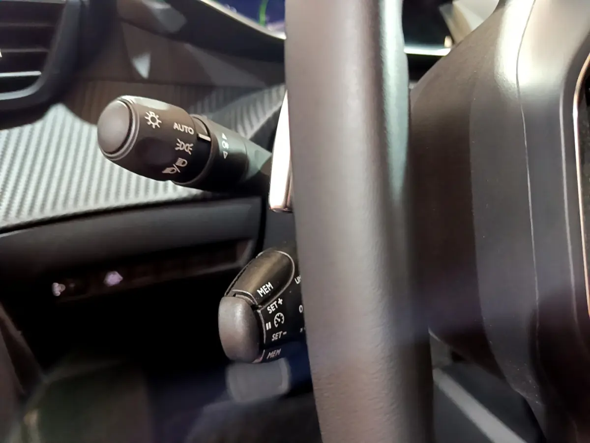 Gros plan sur la commande de régulateur de vitesse et éclairage derrière le volant cuir d'une Peugeot 208 jaune 2023.