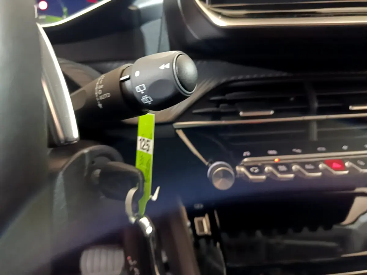 Détail intérieur du tableau de bord de la Peugeot 208 jaune 2023, avec commandes et clé insérée dans le contacteur.