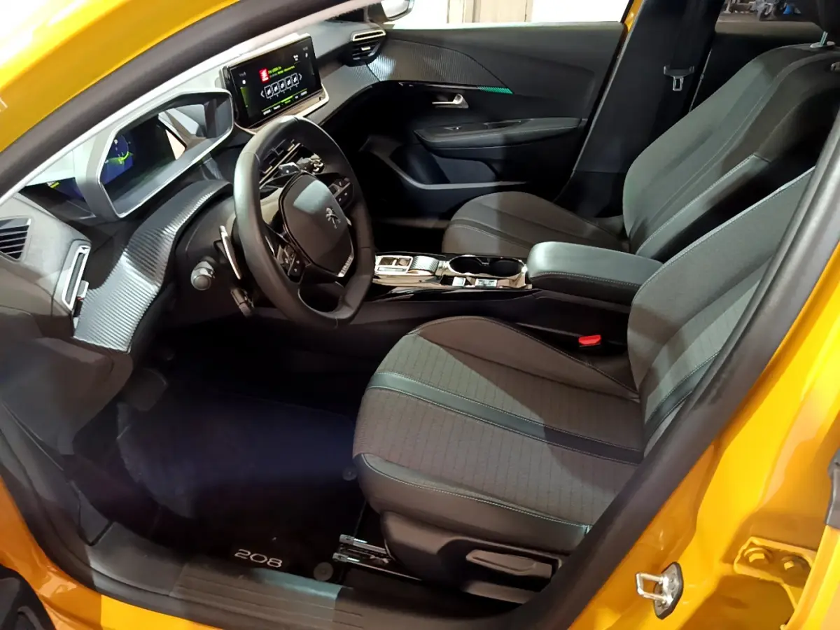 Vue intérieure côté conducteur de la Peugeot 208 jaune 2023, avec tableau de bord digital et sièges tissu gris.