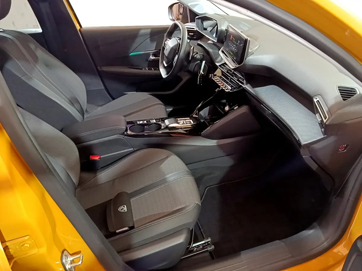 Intérieur avant droit de la Peugeot 208 jaune 2023 avec tableau de bord numérique et sièges gris tissu.