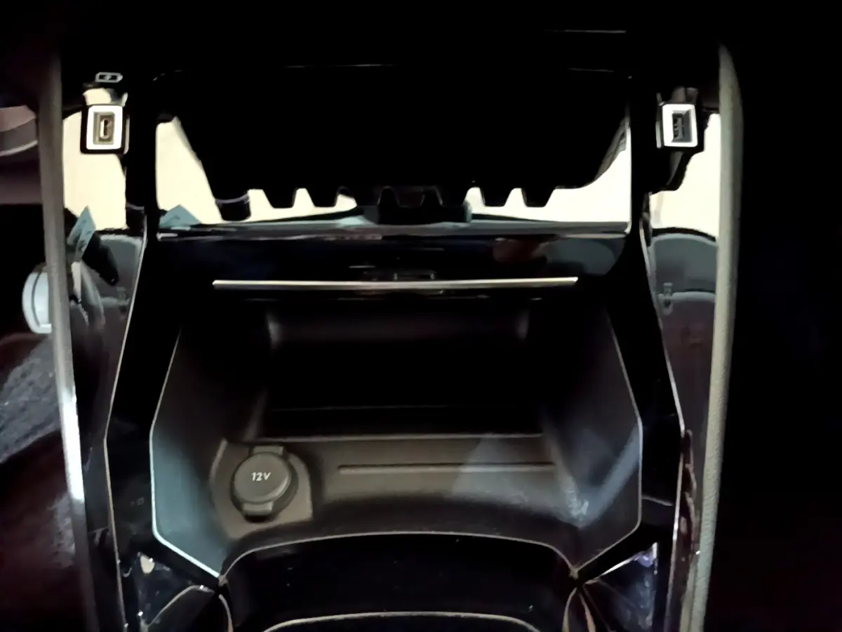 Prise 12V en gros plan dans la console centrale noire de la Peugeot 208 jaune PureTech 2023