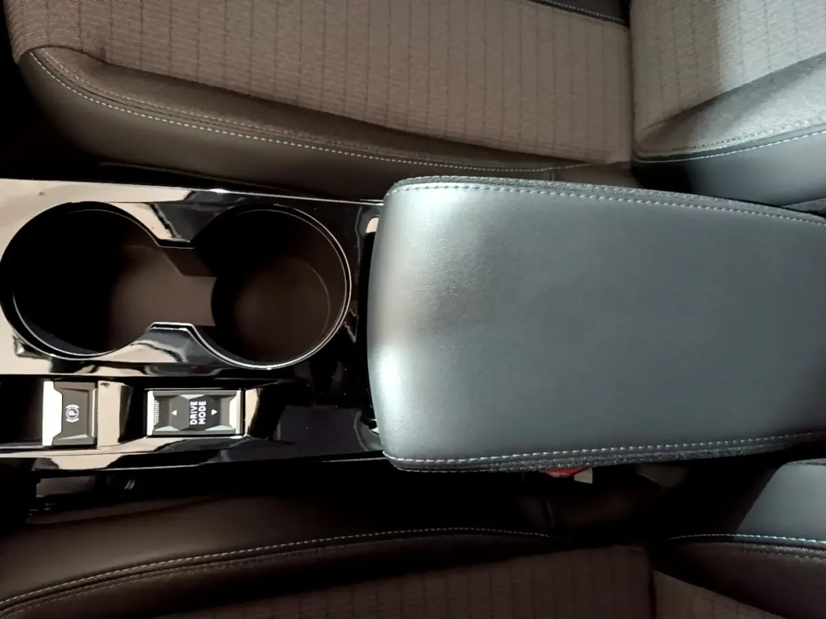 Gros plan sur la console centrale noire avec accoudoir cuir et commandes Drive Mode de la Peugeot 208 jaune 2023.
