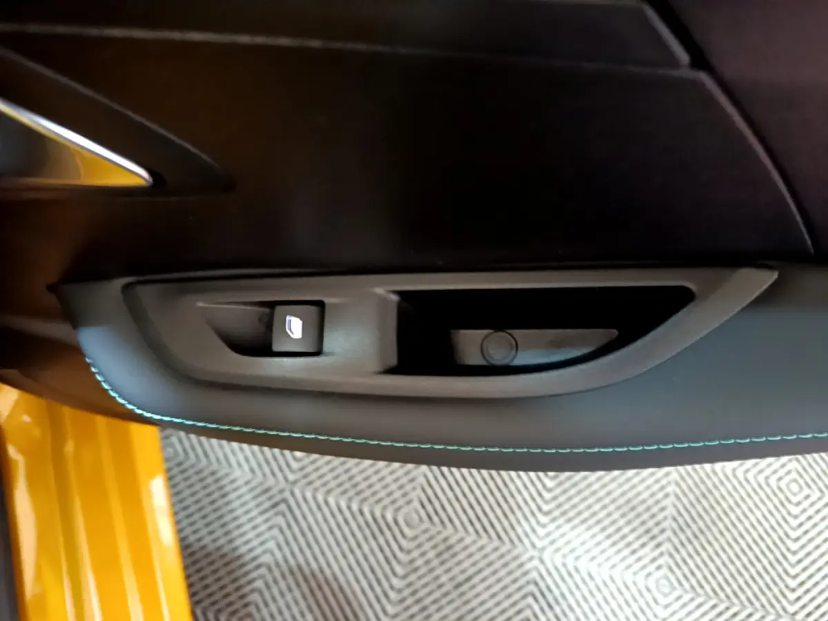 Détail de la commande de lève-vitre côté gauche sur la porte intérieure noire avec surpiqûres bleues d'une Peugeot 208 jaune 2023