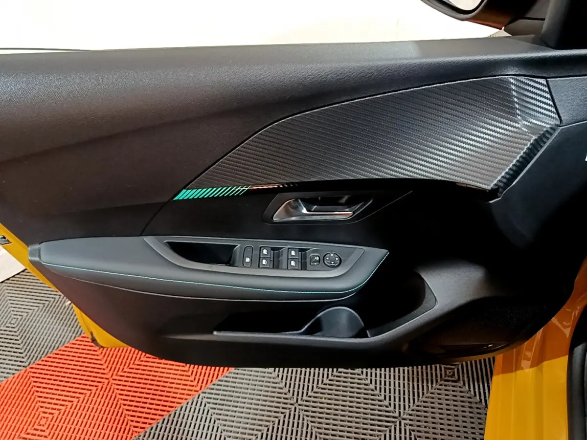 Vue rapprochée de la porte avant gauche noire avec insert effet carbone d'une Peugeot 208 jaune 2023.