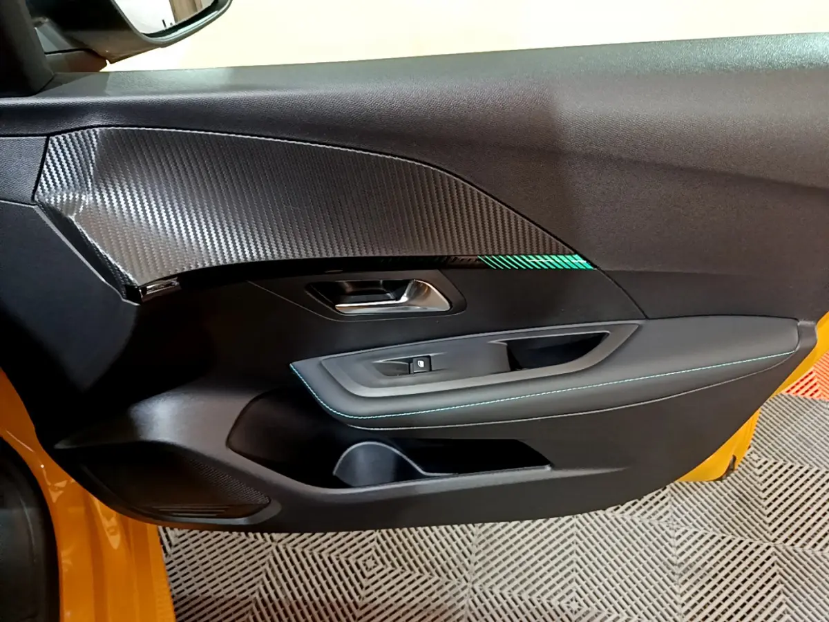 Vue rapprochée de la porte côté gauche jaune de la Peugeot 208 avec insert carbone et surpiqûres bleues.