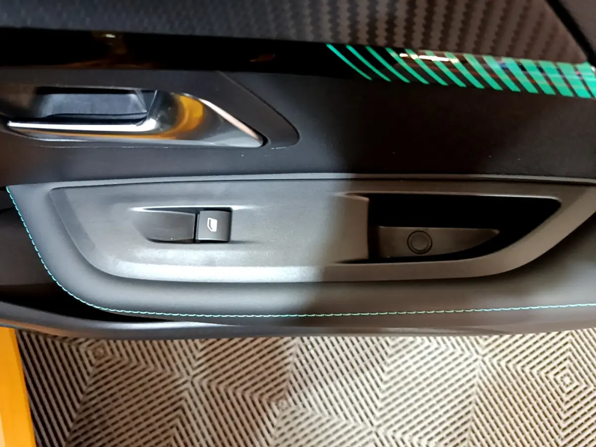 Gros plan sur la poignée intérieure et le bouton de lève-vitre côté gauche de la porte d'une Peugeot 208 jaune.