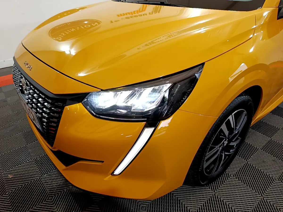 Gros plan sur l'avant droit d'une Peugeot 208 jaune 2023 avec phares LED allumés et calandre noire texturée