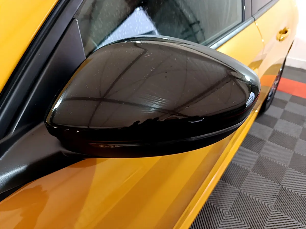 Rétroviseur noir côté gauche d'une Peugeot 208 jaune vue en gros plan sur fond intérieur.