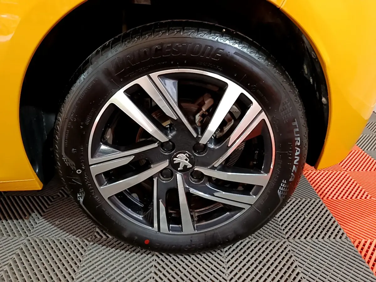 Gros plan sur la roue avant gauche de la Peugeot 208 jaune avec jante alliage noire et argentée distinctive.