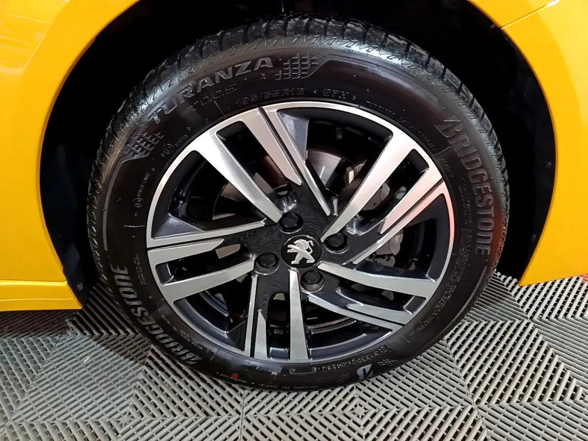 Gros plan sur la roue avant droite de la Peugeot 208 jaune 2023 avec jante alliage bicolore et pneu Bridgestone.