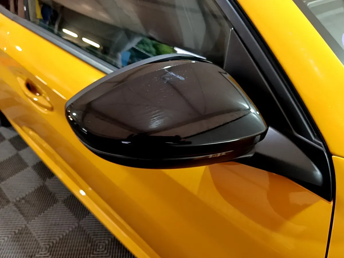 Rétroviseur noir brillant côté conducteur d'une Peugeot 208 jaune vue de près sur porte avant.
