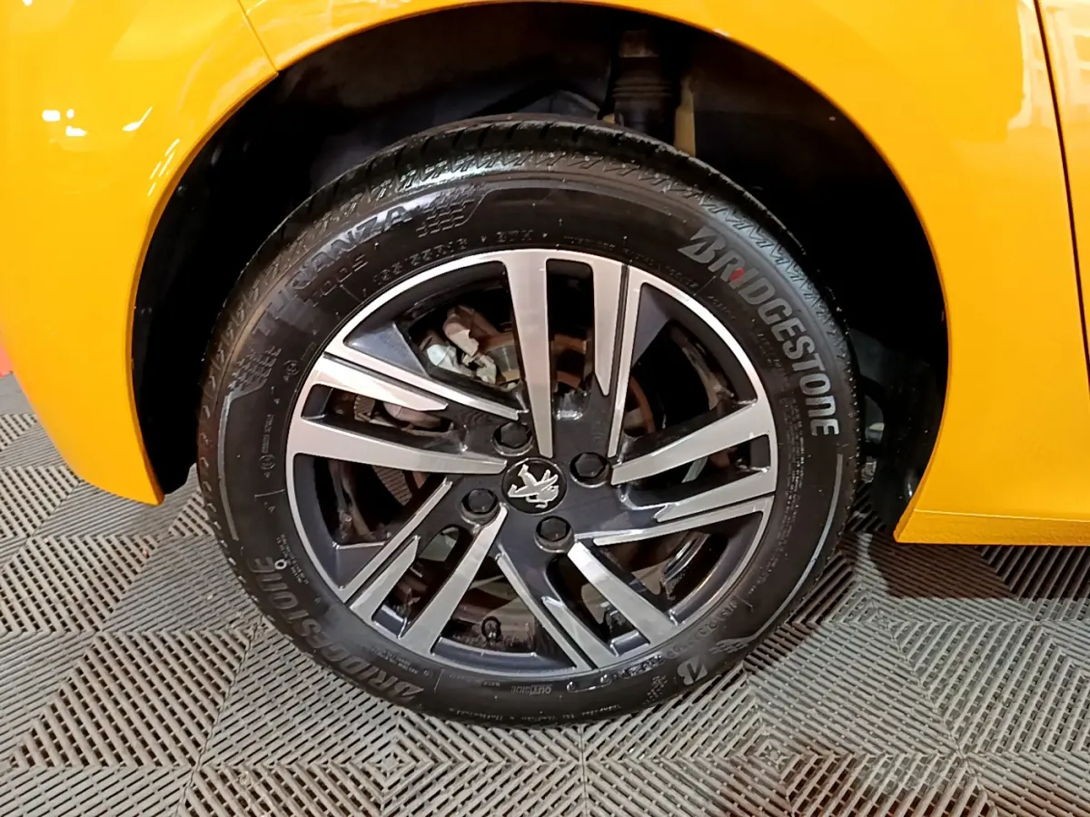 Gros plan sur la roue avant gauche d'une Peugeot 208 jaune 2023 avec jante alliage et pneu Bridgestone.