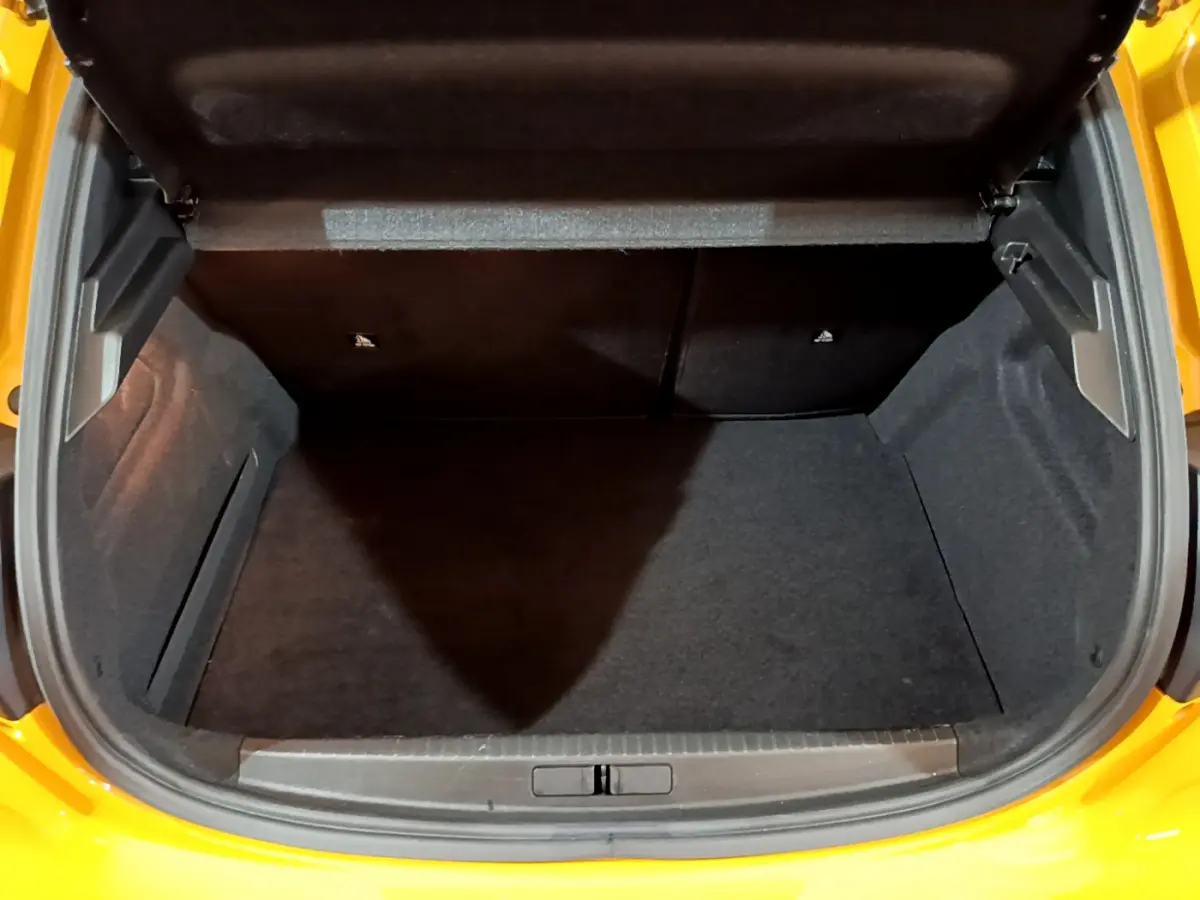 Coffre ouvert vu de l'arrière d'une Peugeot 208 jaune 2023, espace de chargement vide et tapis noir.