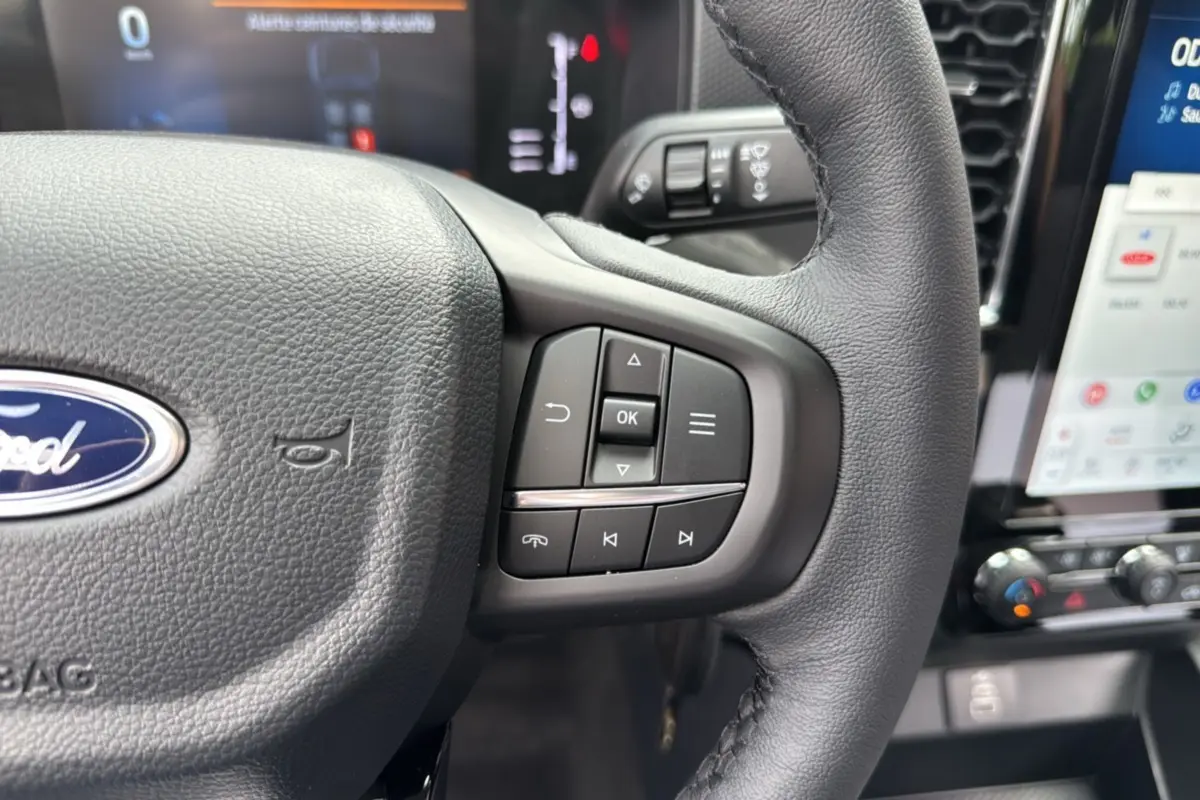 Gros plan sur le volant en cuir du Ford Ranger gris carbone 2025, avec commandes intégrées et tableau de bord numérique visible.