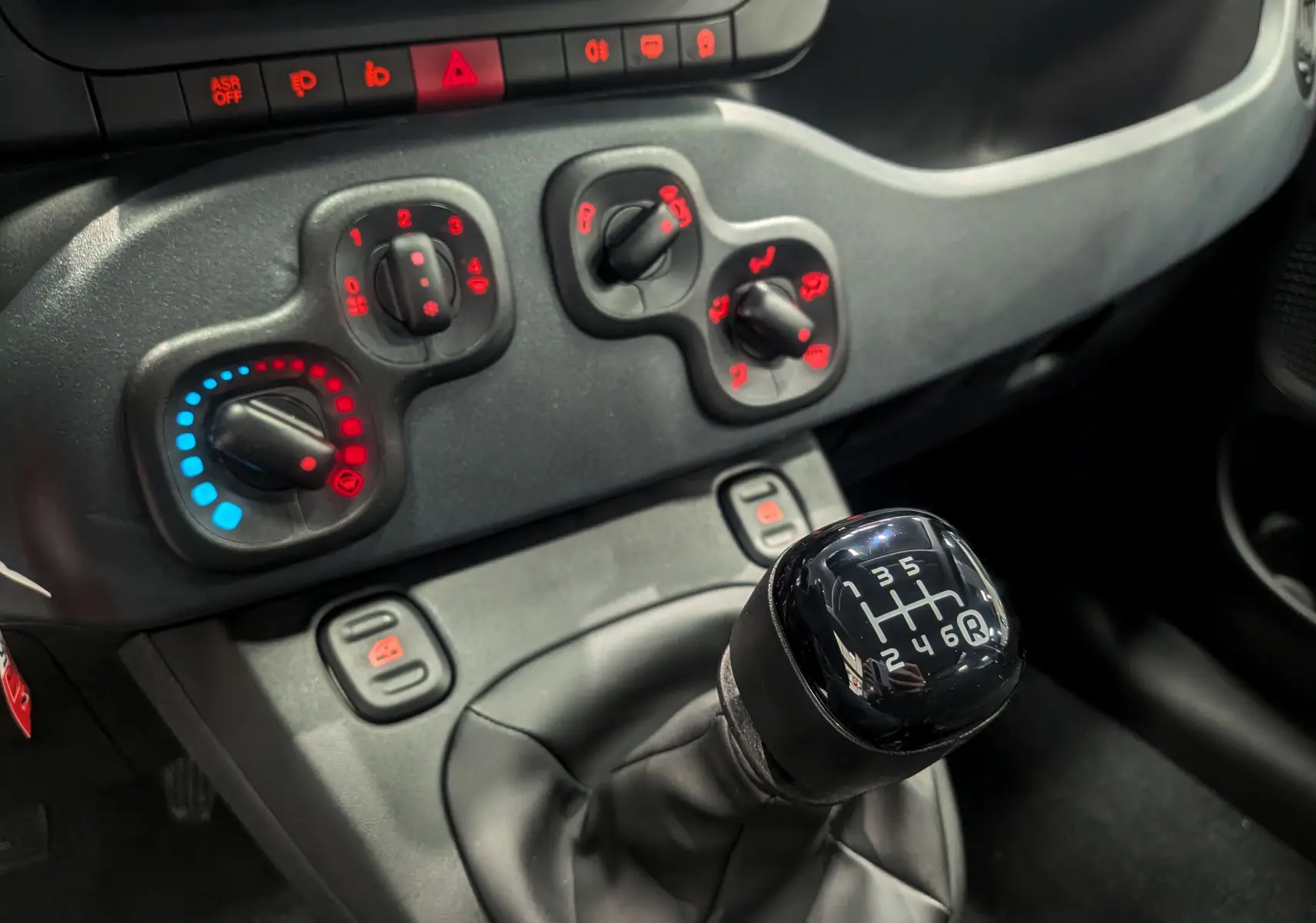 Gros plan sur la boîte manuelle noire et les commandes de climatisation rouges et bleues de la Fiat Panda 2025.