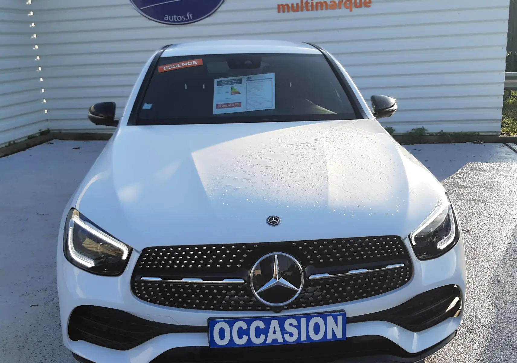 Affiche de promotion orange et bleue posée sur le capot blanc d'une Mercedes GLC Coupé 300 4MATIC AMG vue de près.